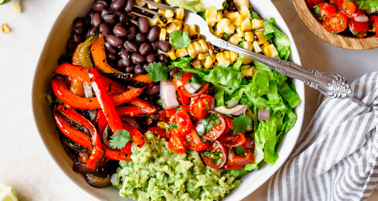 An aerial image of a colorful salad with peppers, black beans, corn, lettuce, tomatoes. and guacamole. 