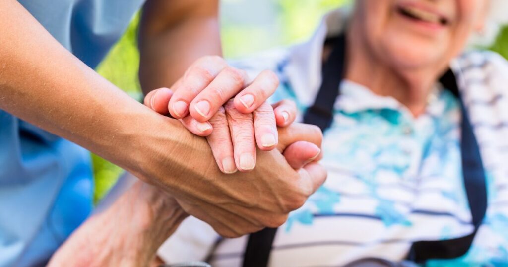 Elderly woman holding the hands of a nurse outside.